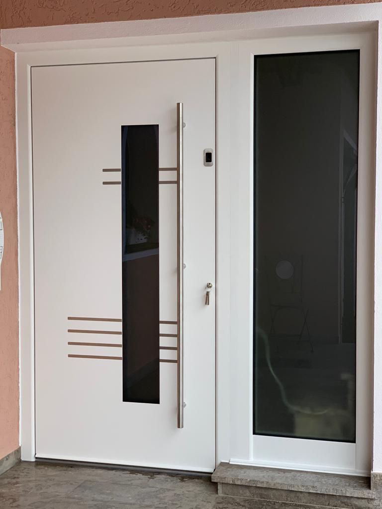 Weiße Haustür mit dunkler Glasscheibe und Seitenlicht, Edelstahlgriff und horizontalen Linien.