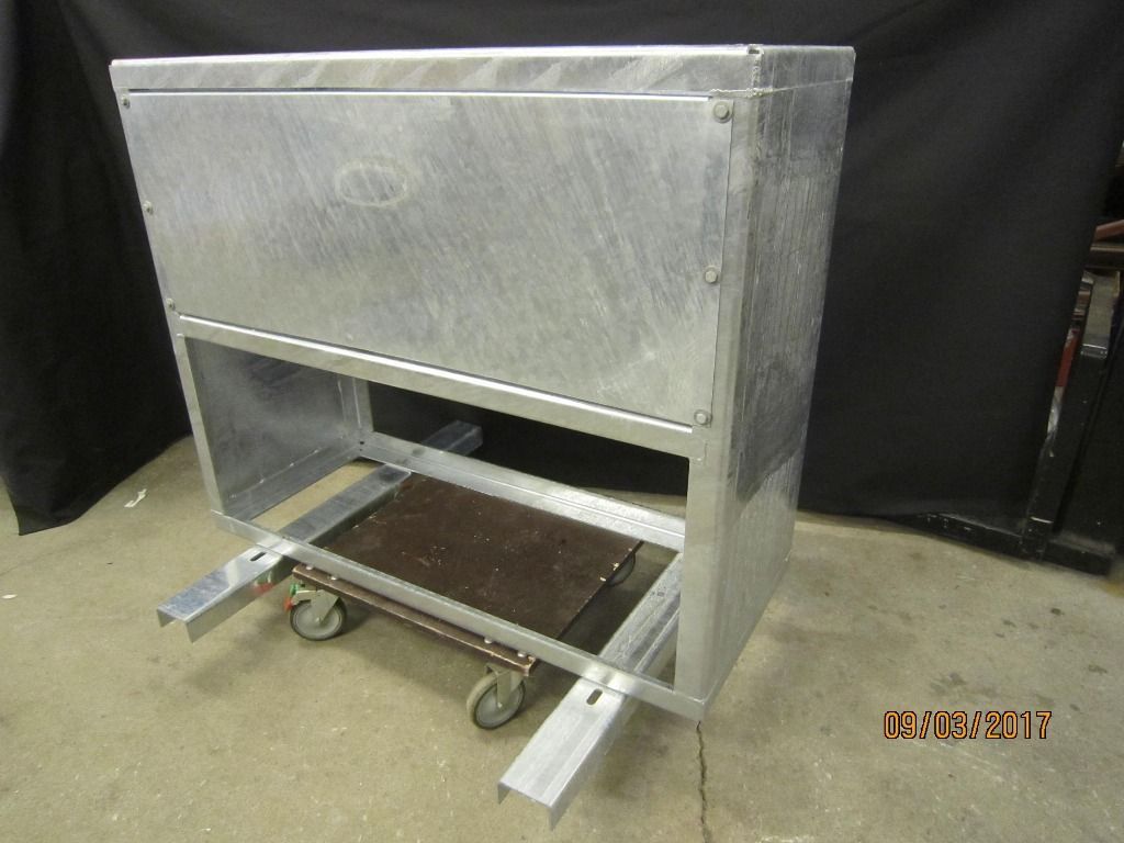Tummaa taustaa vasten esitetty metallikärry, jossa on suuri hopeinen pyörillä varustettu kotelo.