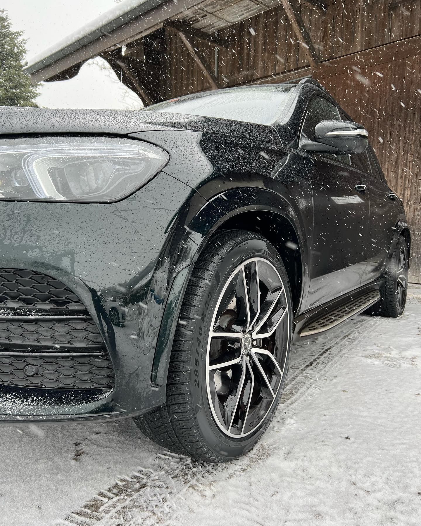 Ein schwarzes Auto parkt im Schnee vor einem Holzgebäude.
