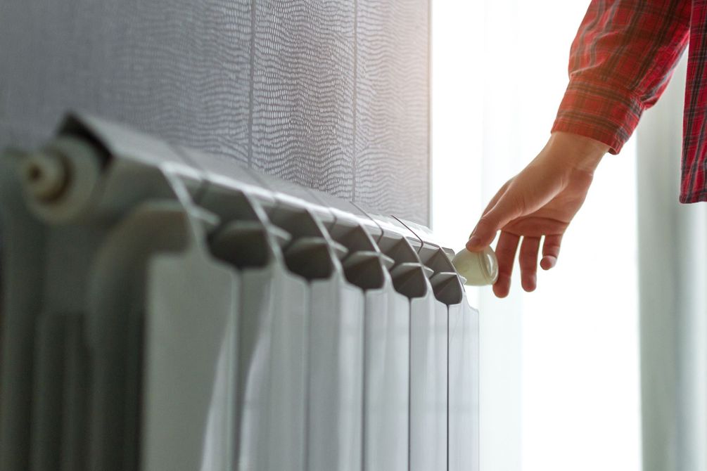 Une main règle le robinet d'un radiateur près d'une fenêtre.