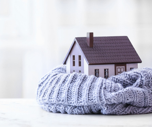 Maquette de petite maison nichée dans une épaisse écharpe tricotée sur une surface.
