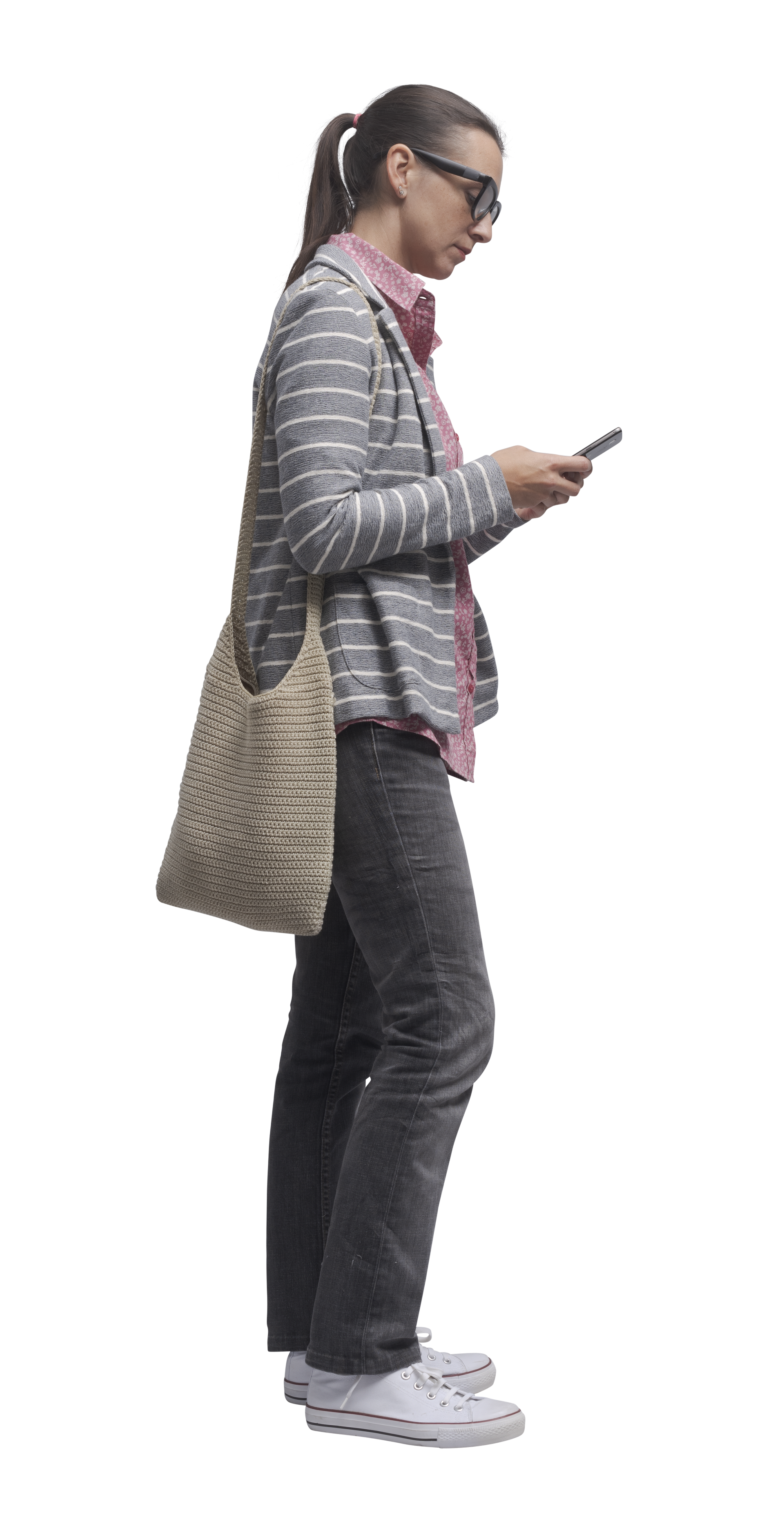 Une personne vêtue d'une veste et d'un pantalon regarde son téléphone et porte un sac fourre-tout en osier.