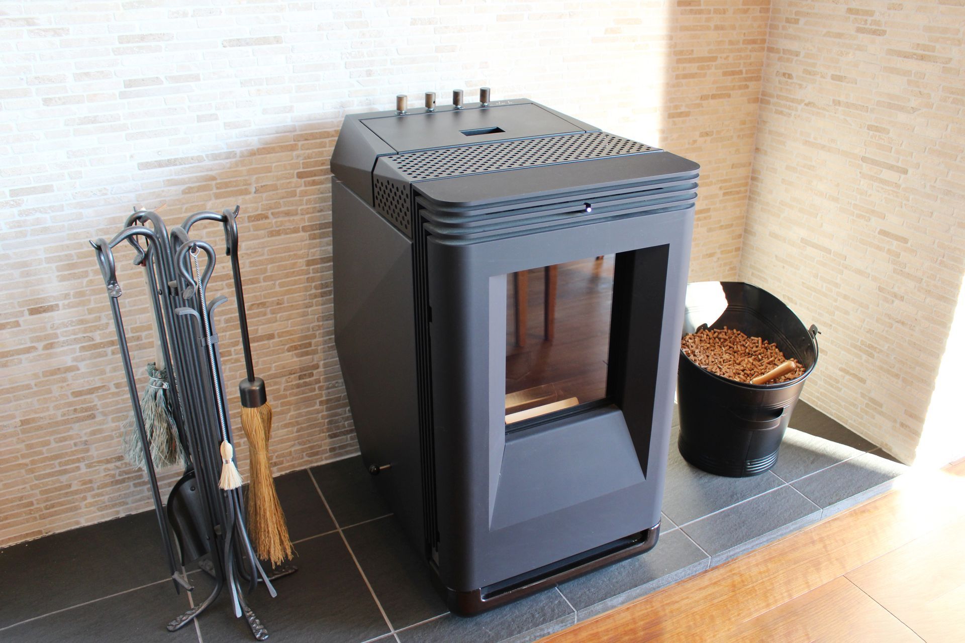 Poêle à bois avec accessoires de cheminée et un seau de bois de chauffage sur un foyer carrelé.