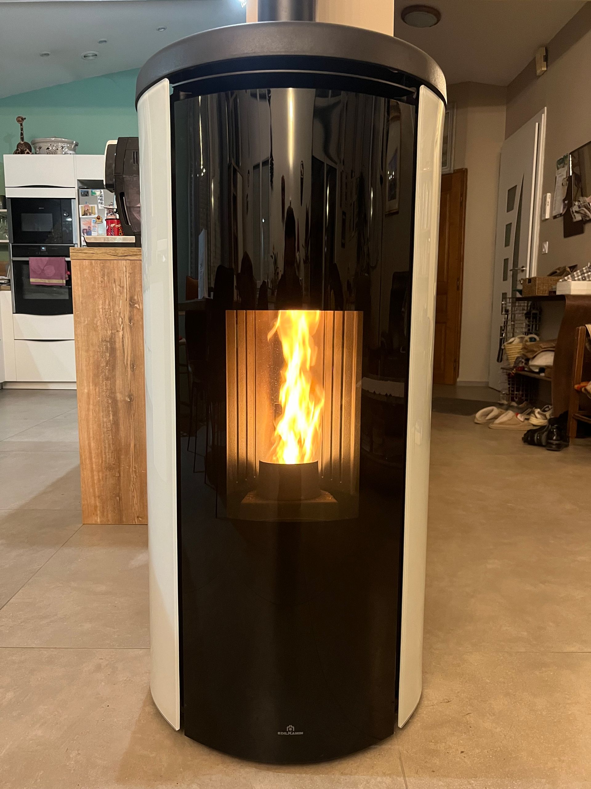 Poêle à granulés cylindrique avec flamme visible à l'intérieur d'une maison.
