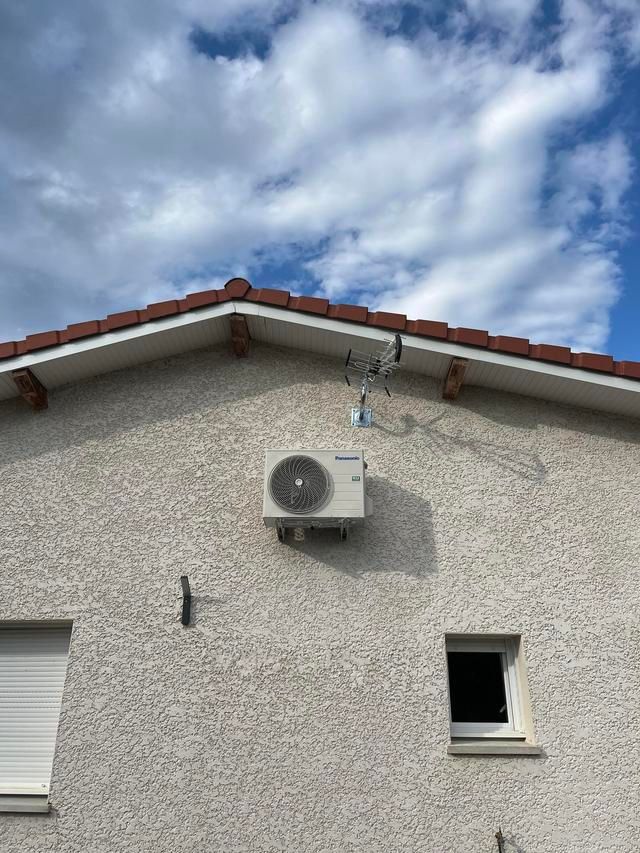 Façade de maison avec un climatiseur mural sous un toit de tuiles.