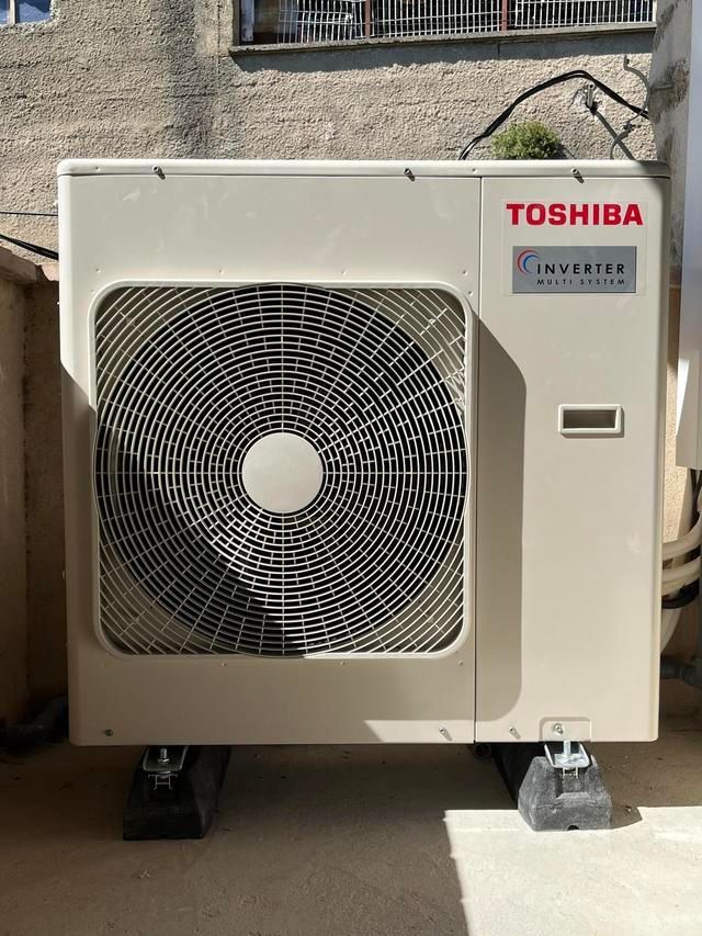 Unité de climatisation extérieure Toshiba fixée au mur, avec une grande grille de ventilateur.