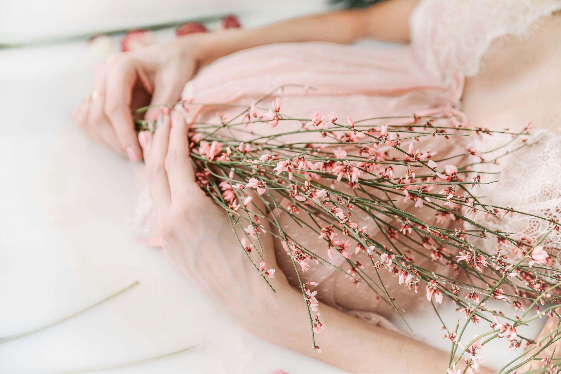 Persona sosteniendo un ramo de delicadas flores rosas y blancas sobre una tela blanca suave.
