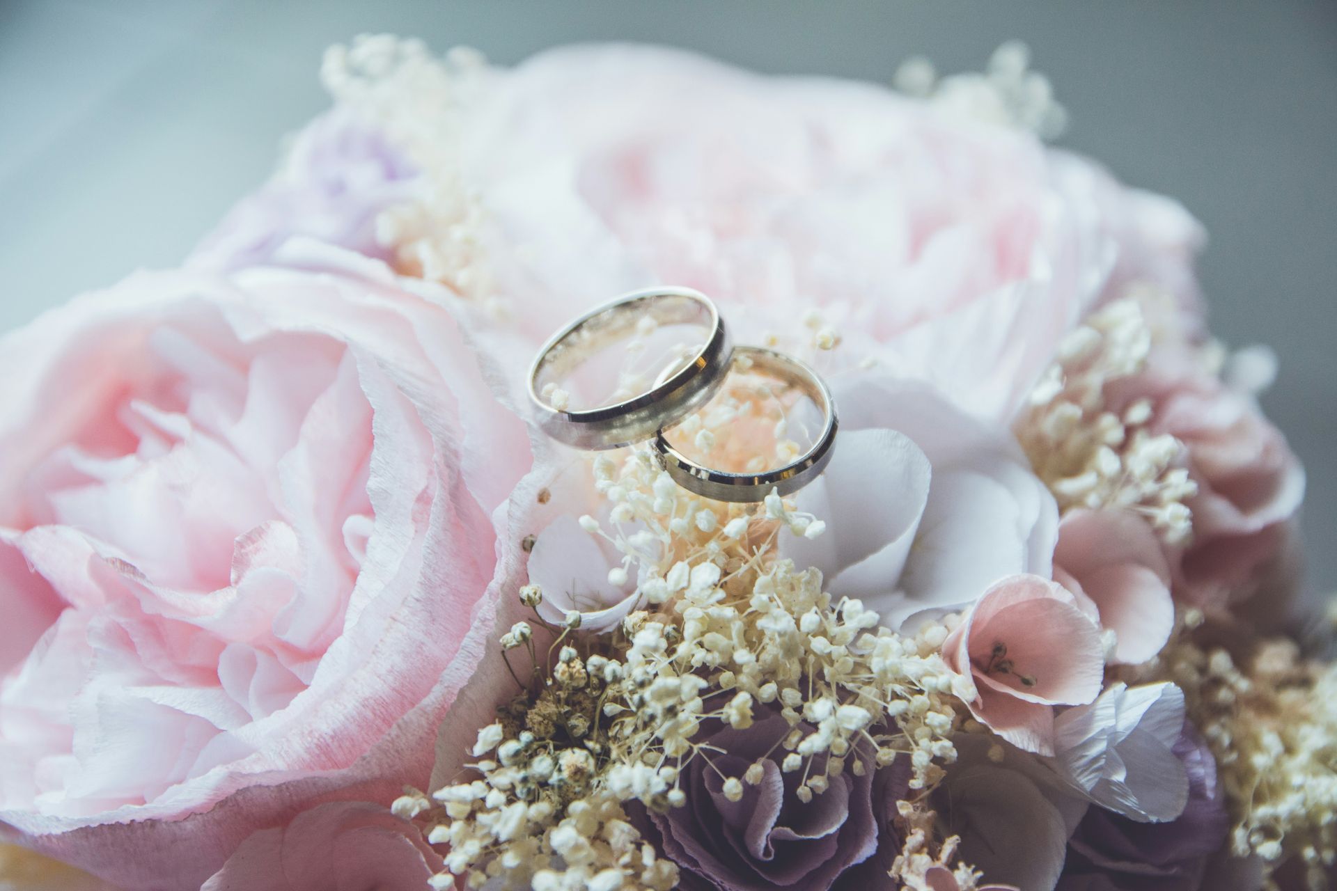 Dos anillos de boda engastados en un ramo floral rosa pastel con perlas.