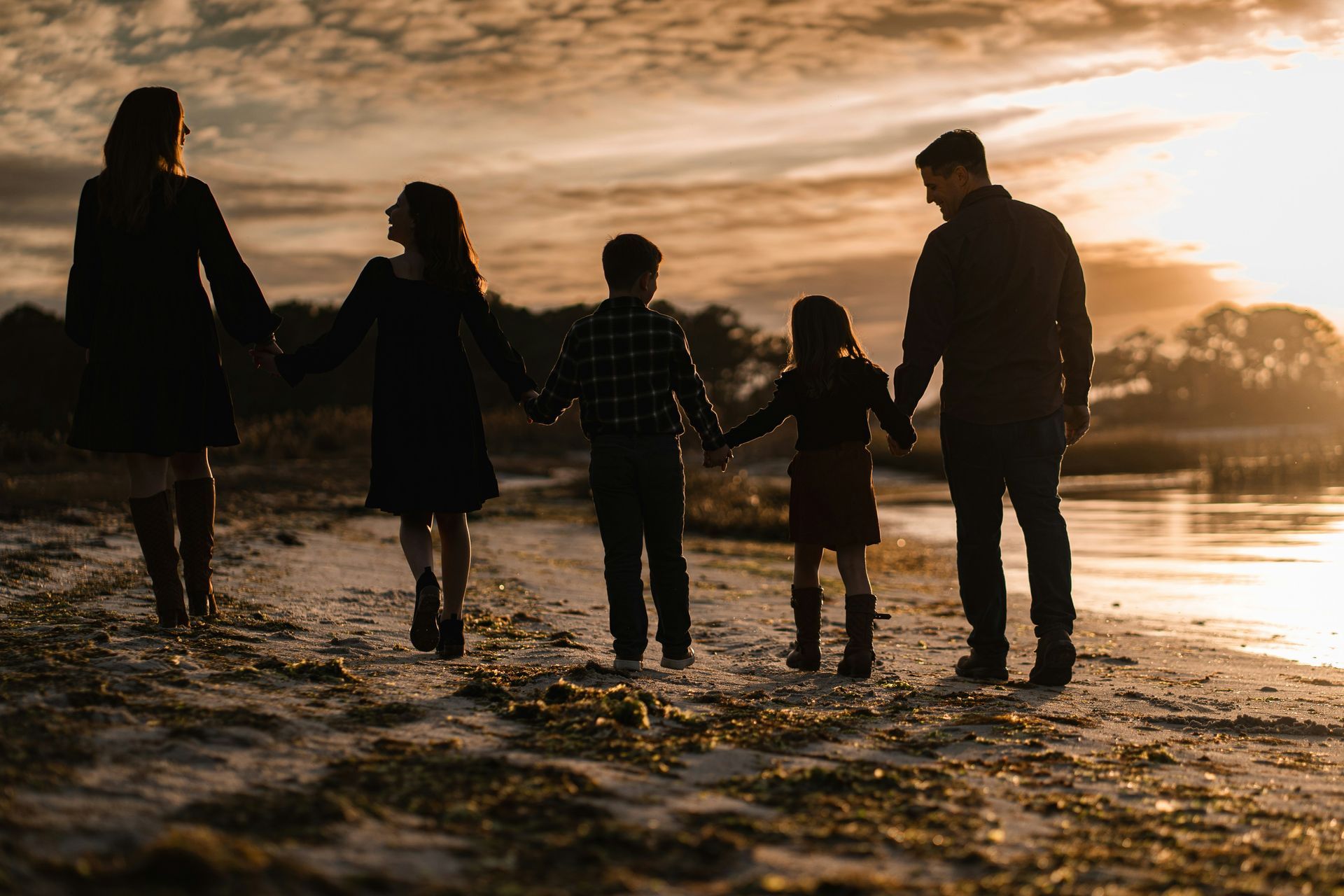 Familia en silueta tomada de la mano en una playa al atardecer, caminando por la orilla.
