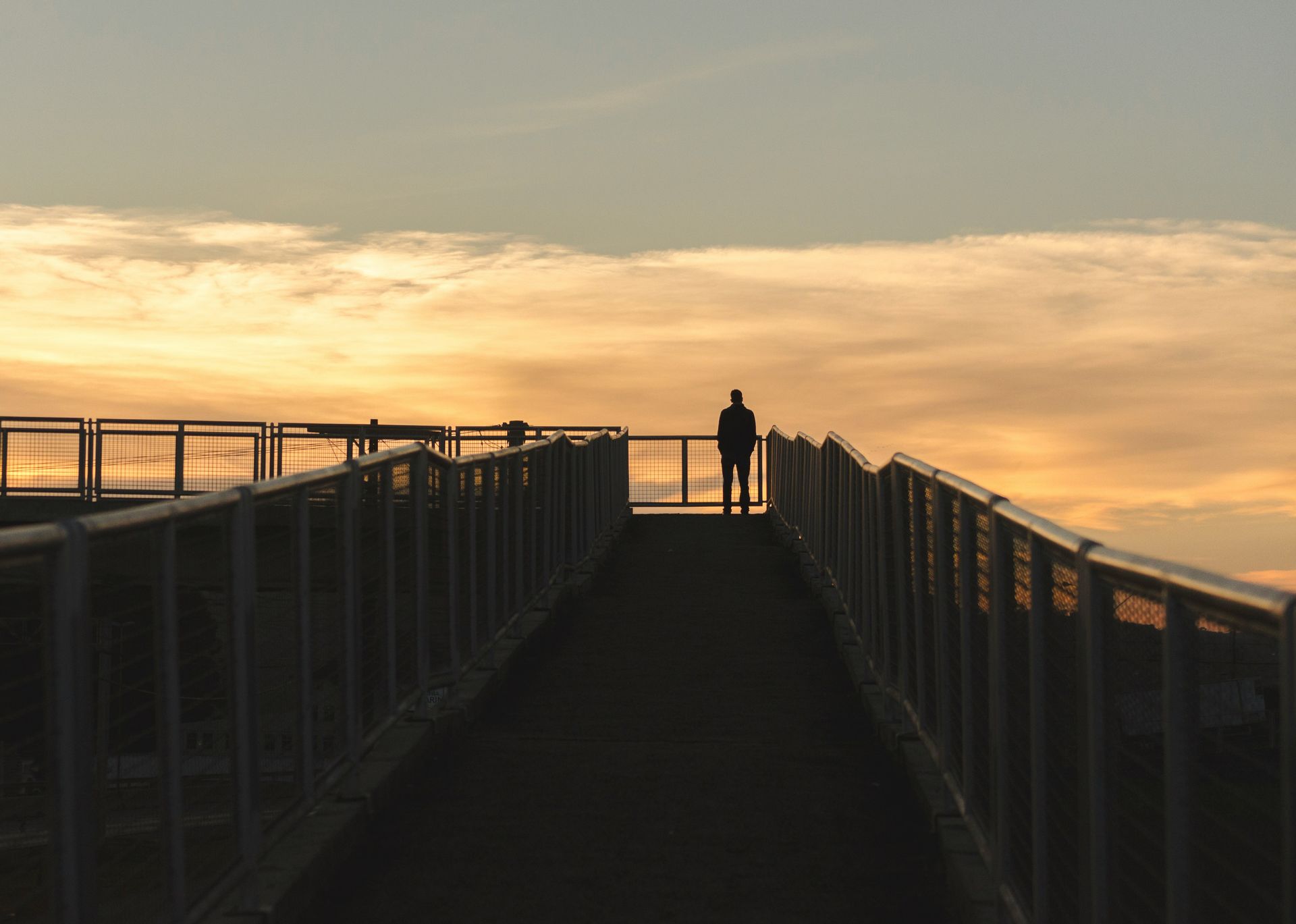 Silueta de una persona en lo alto de una pasarela de un puente al atardecer.