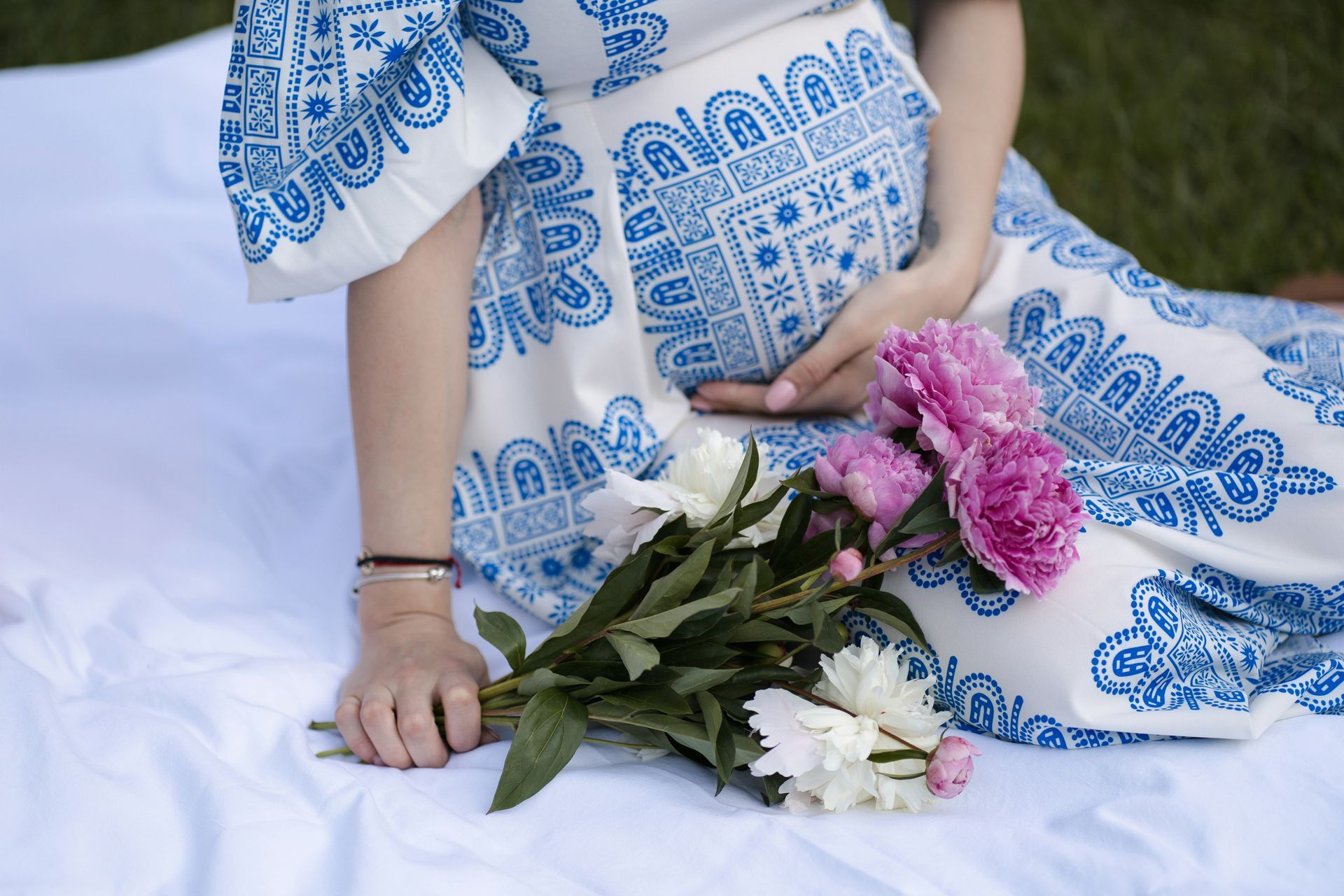 Una persona con un vestido azul estampado sostiene un ramo de flores rosas y blancas sobre una cama blanca.