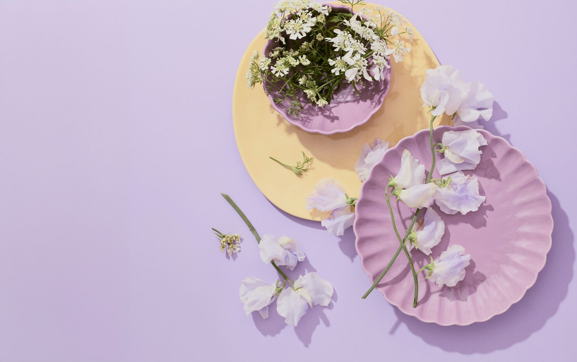 Arreglo floral en tonos pastel con flores blancas sobre círculos de papel en forma de abanico de color amarillo y rosa.