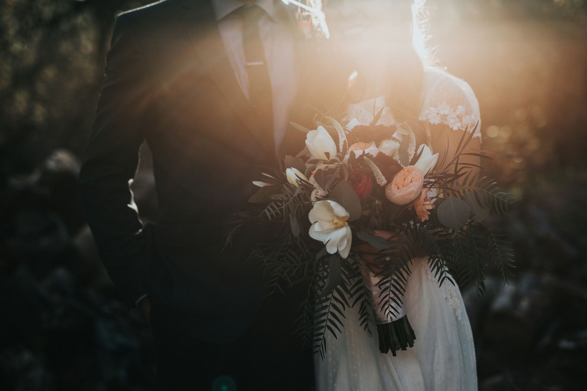 Novia sosteniendo un ramo de flores blancas y rosas bajo la cálida luz del sol al aire libre.