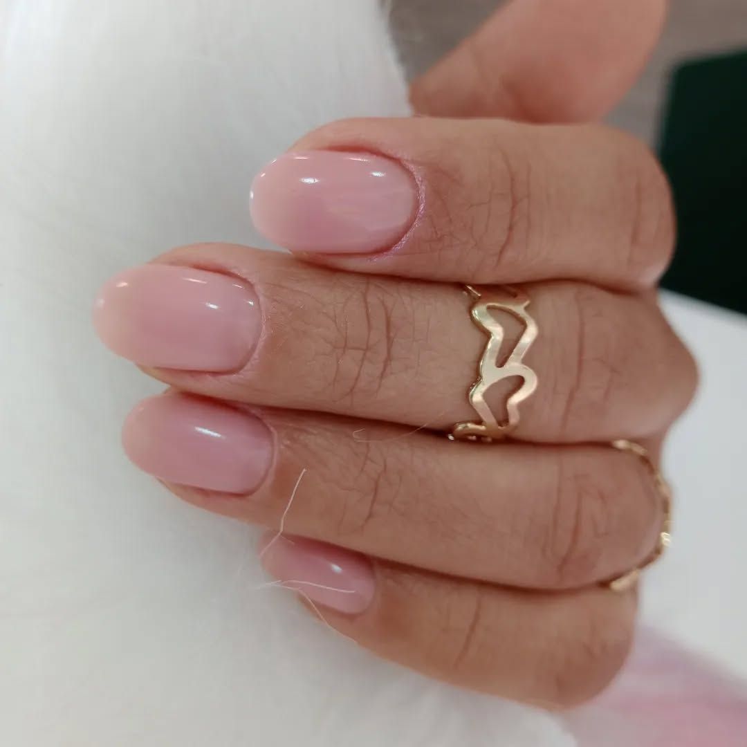 La mano de una mujer con uñas rosas y un anillo de oro en el dedo.