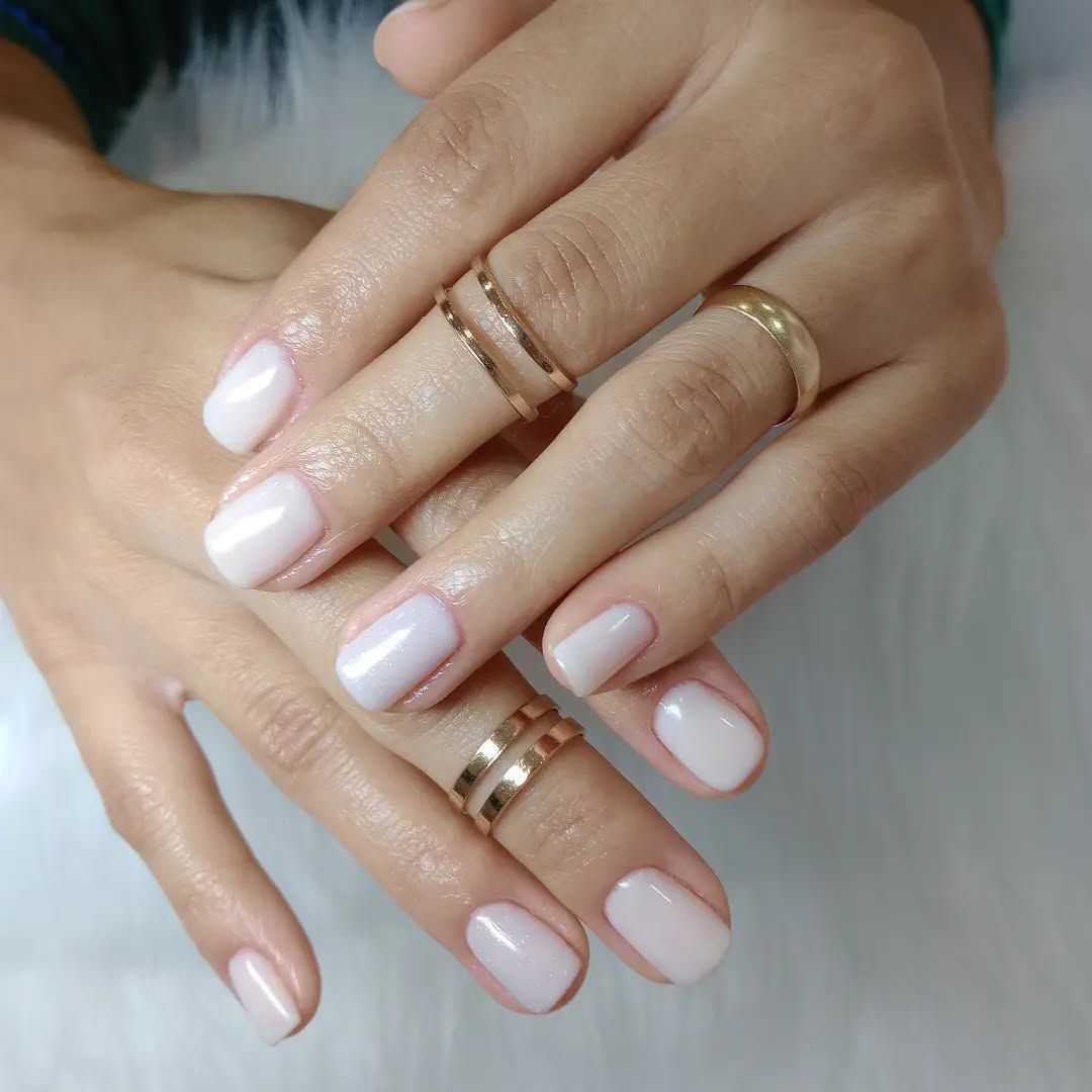 Manos de mujer con uñas blancas y anillos en los dedos.