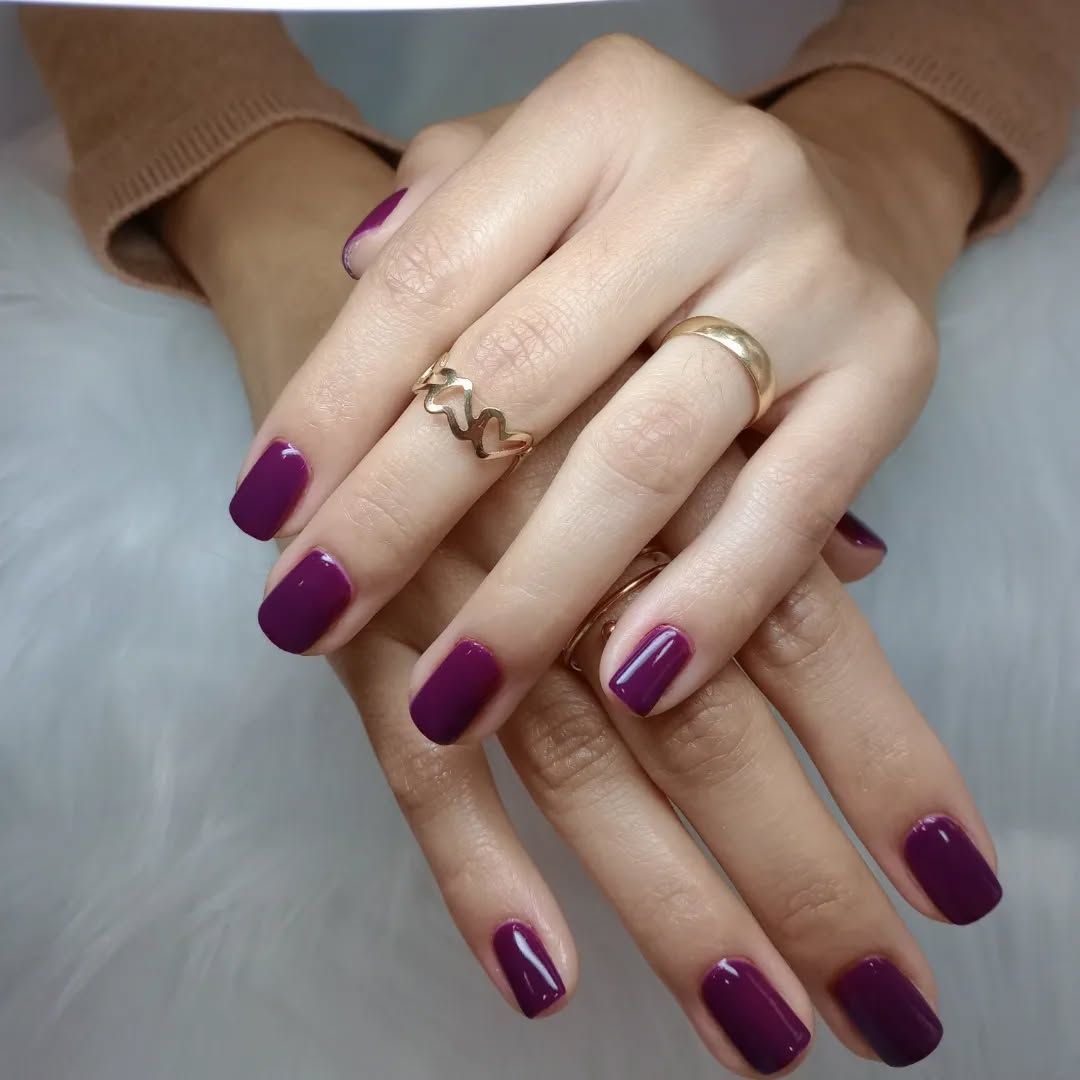 Manos de mujer con uñas moradas y un anillo de oro.