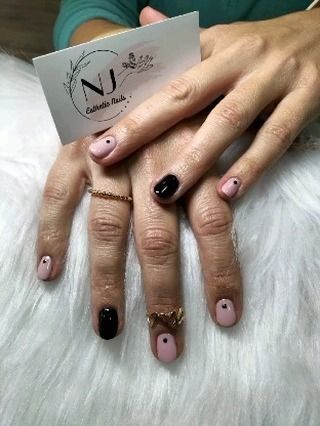 Unas manos de mujer con uñas negras y rosas y un anillo.