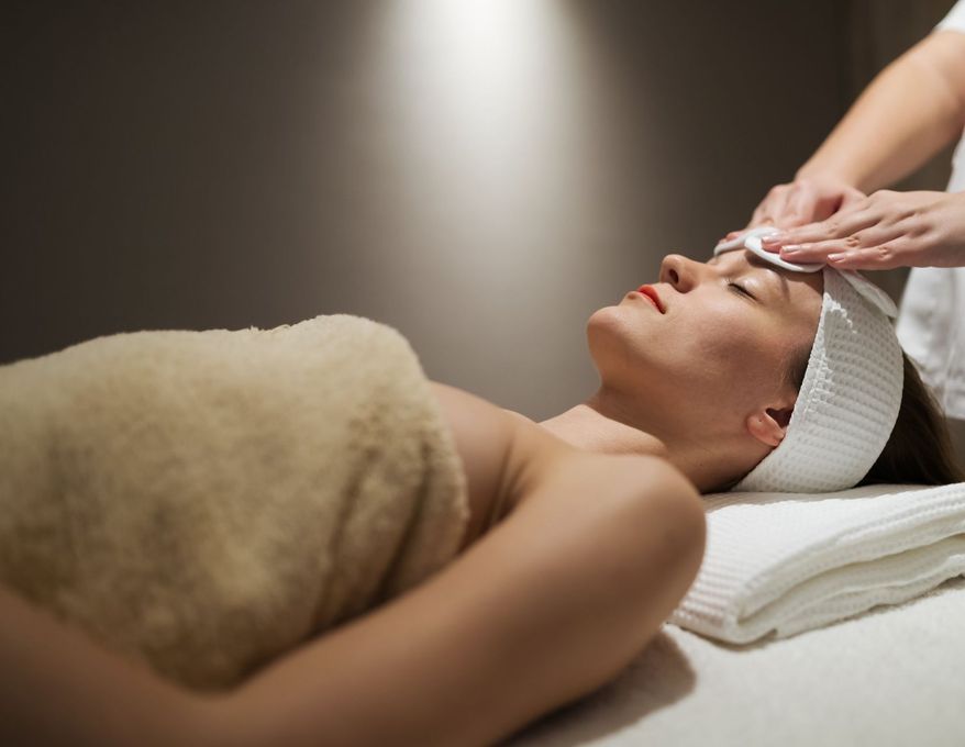 Una mujer envuelta en una toalla está recibiendo un tratamiento facial en un spa.