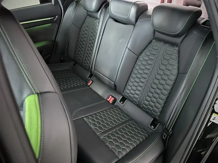 Asiento trasero de coche negro con costuras estampadas y paneles decorativos verdes.