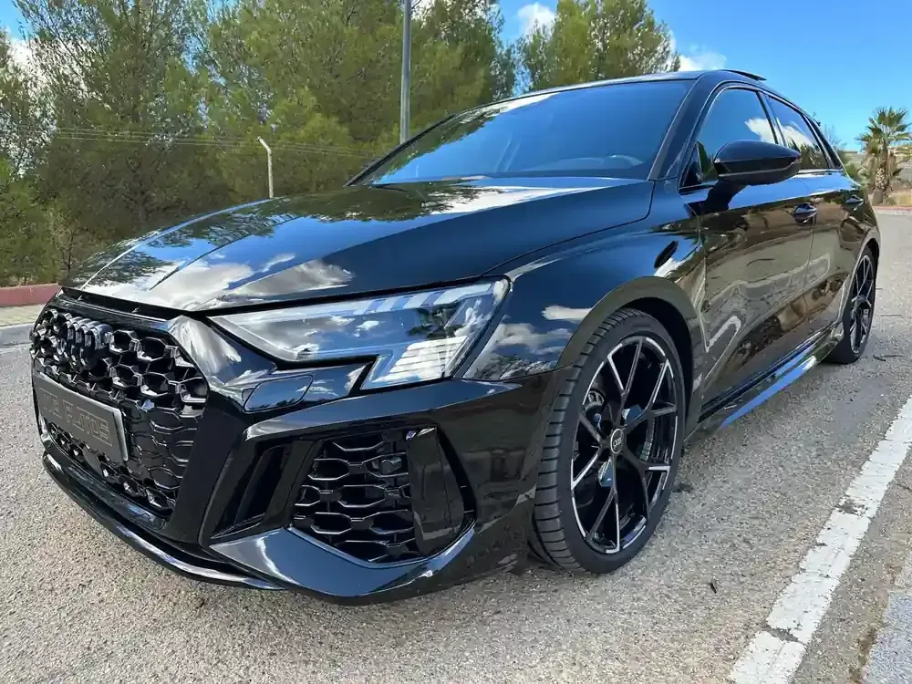 Coche deportivo compacto negro aparcado al borde de la carretera, visto desde la parte delantera.
