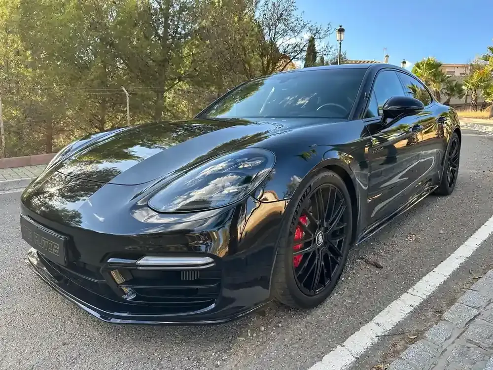 Un Porsche deportivo negro aparcado en una calle con árboles y reflejos de la luz del sol.