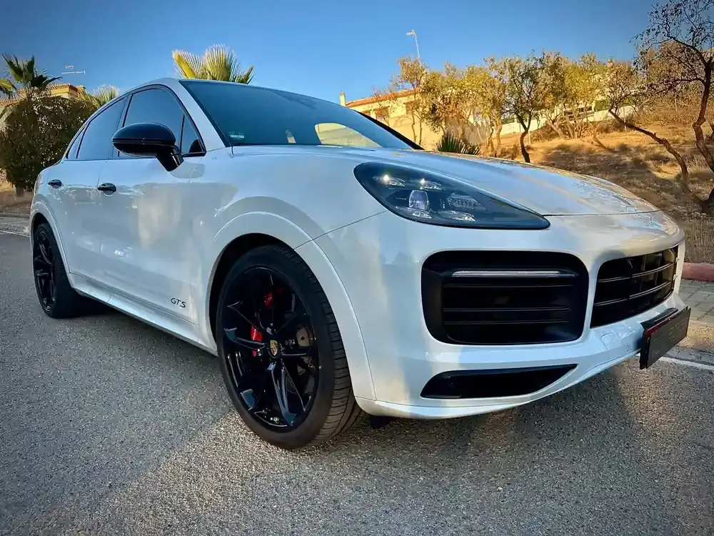 Un SUV blanco estacionado en una carretera soleada, con ruedas negras y árboles del desierto al fondo.