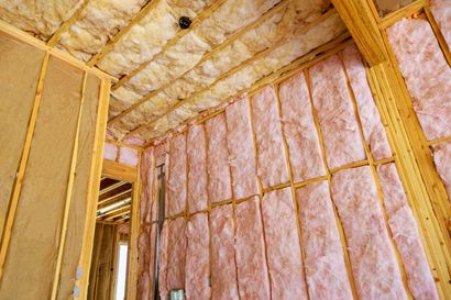 Ossature des murs intérieurs avec isolation rose et montants en bois apparents sous un plafond partiellement isolé