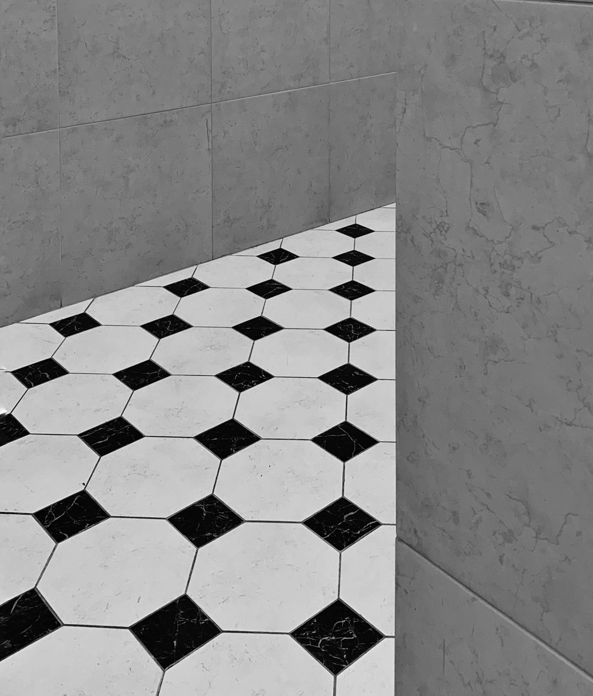 Un sol carrelé noir et blanc rencontre des murs carrelés gris dans un coin