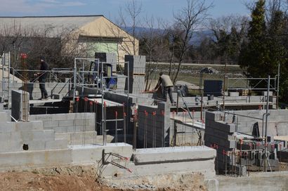 Chantier de construction avec des ouvriers sur des échaffaudages qui bâtissent des murs en parpaings.