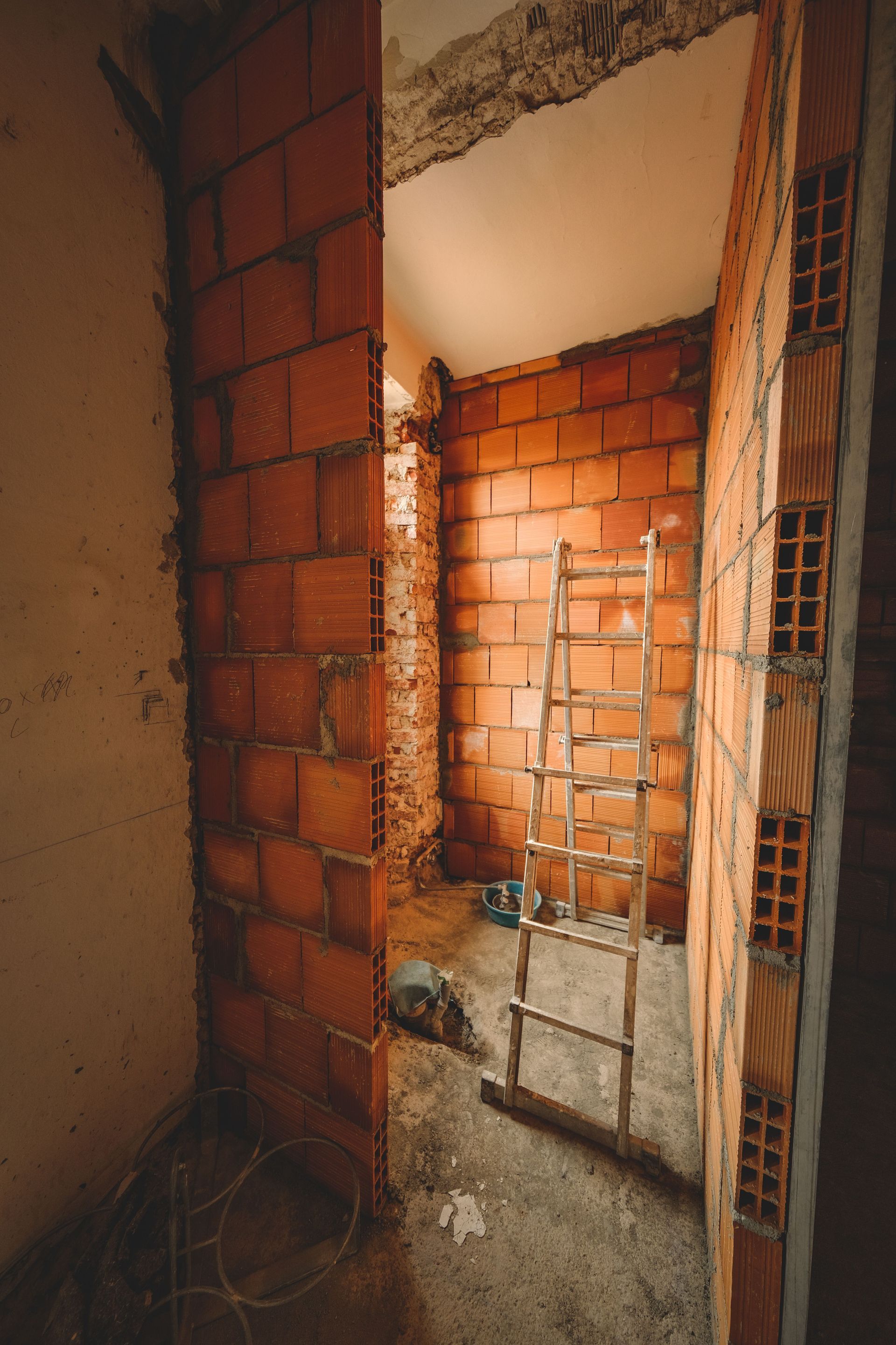 Porte en briques partiellement construite donnant sur une petite pièce inachevée avec des pierres apparentes et des débris au sol