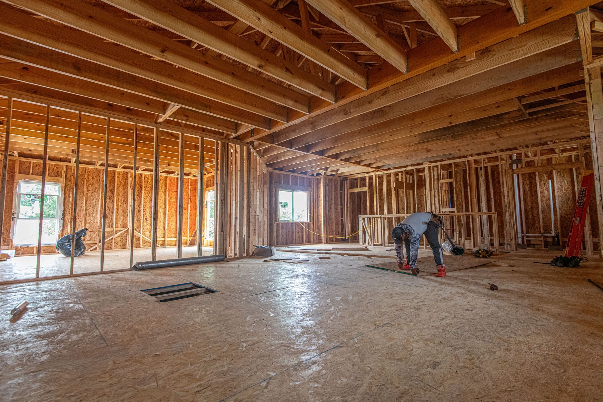 Intérieur d'une maison à ossature en bois en construction, avec des ouvriers et des poutres apparentes.