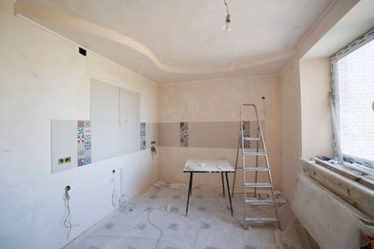 Pièce partiellement rénovée avec échelle, table et murs plâtrés près d'une fenêtre