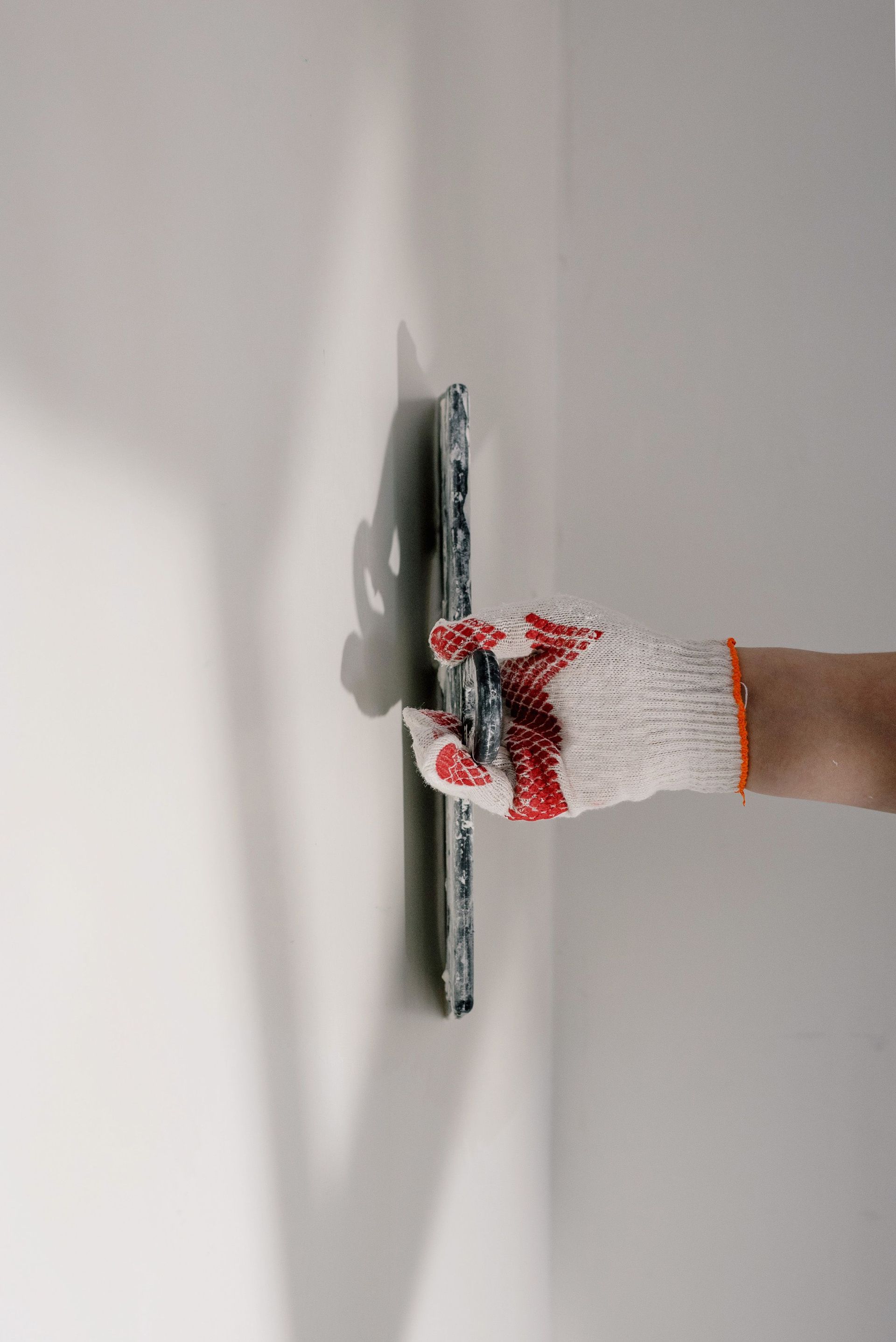 Main gantée lissant de la peinture blanche sur un mur avec un couteau à mastic