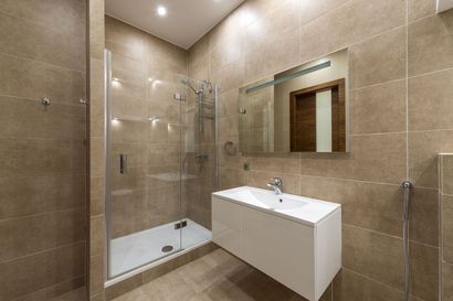 Salle de bains moderne beige avec douche en verre, lavabo mural et miroir
