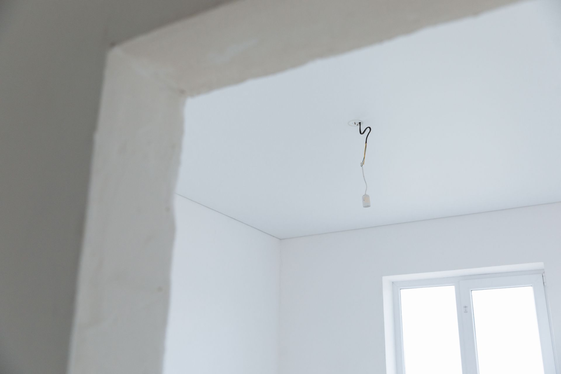 Intérieur d'une pièce blanche avec un fil électrique suspendu au plafond et une fenêtre sur la droite.