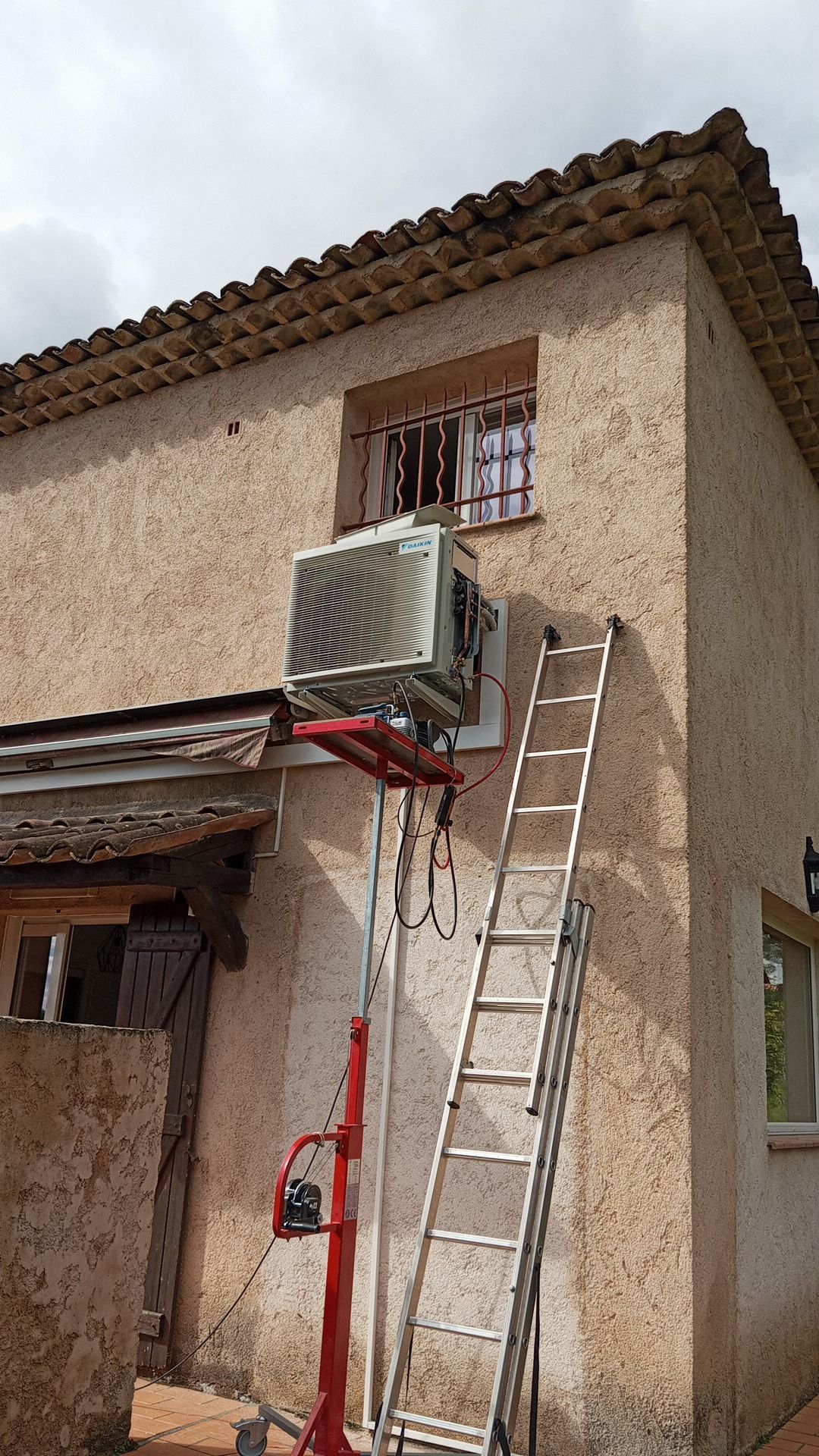 Un climatiseur est monté sur le mur d'un bâtiment, avec une échelle et un ascenseur à proximité.