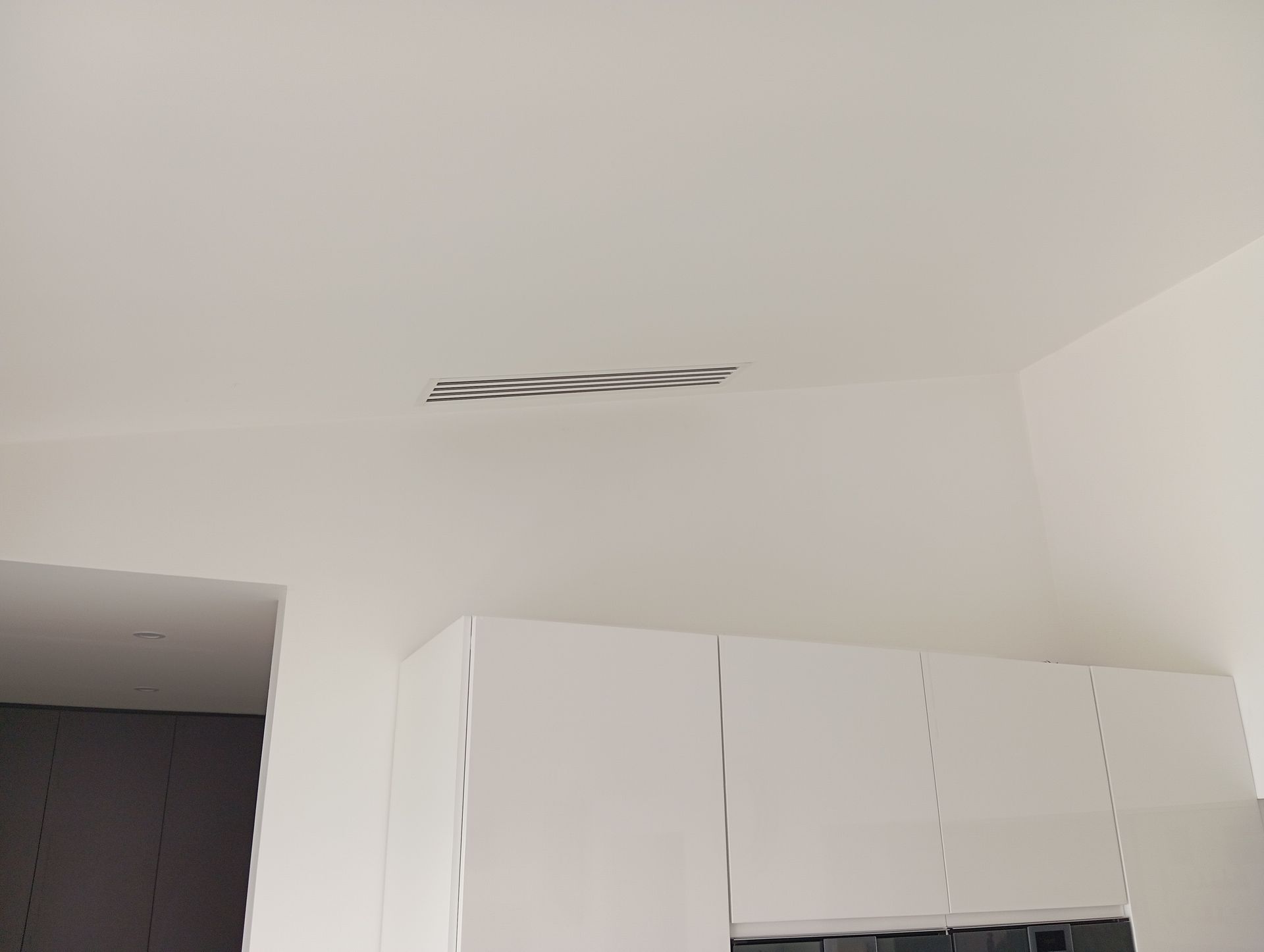 Plafond de cuisine blanc avec une ventilation encastrée au-dessus des armoires blanches.
