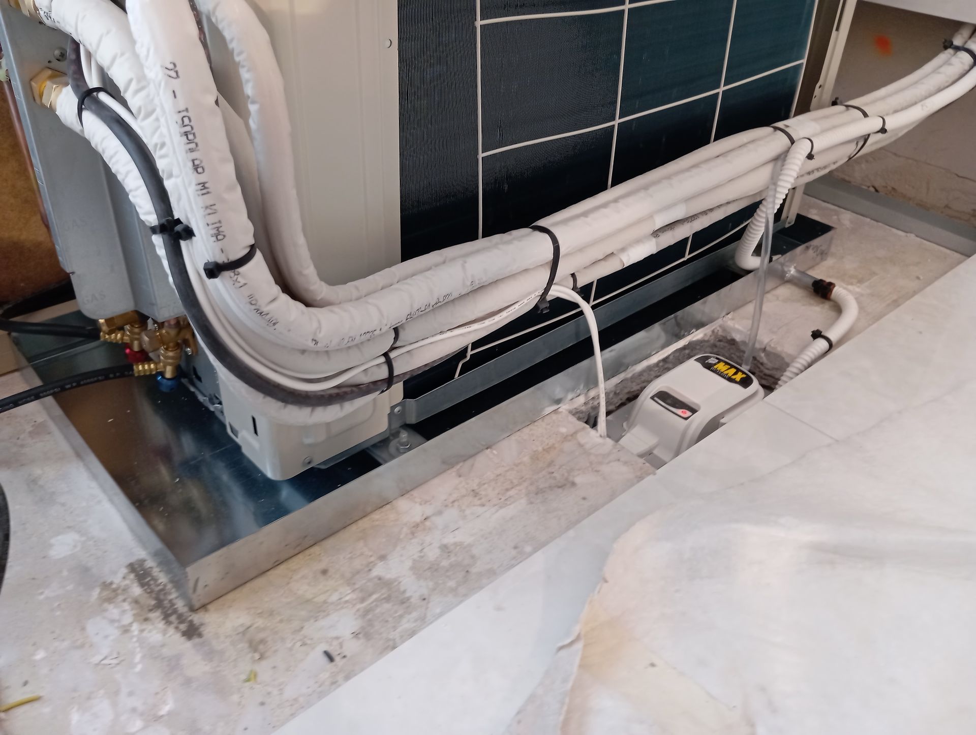 Un climatiseur sur une plateforme métallique ; tuyaux blancs isolés ; mur gris avec une pompe à condensats.