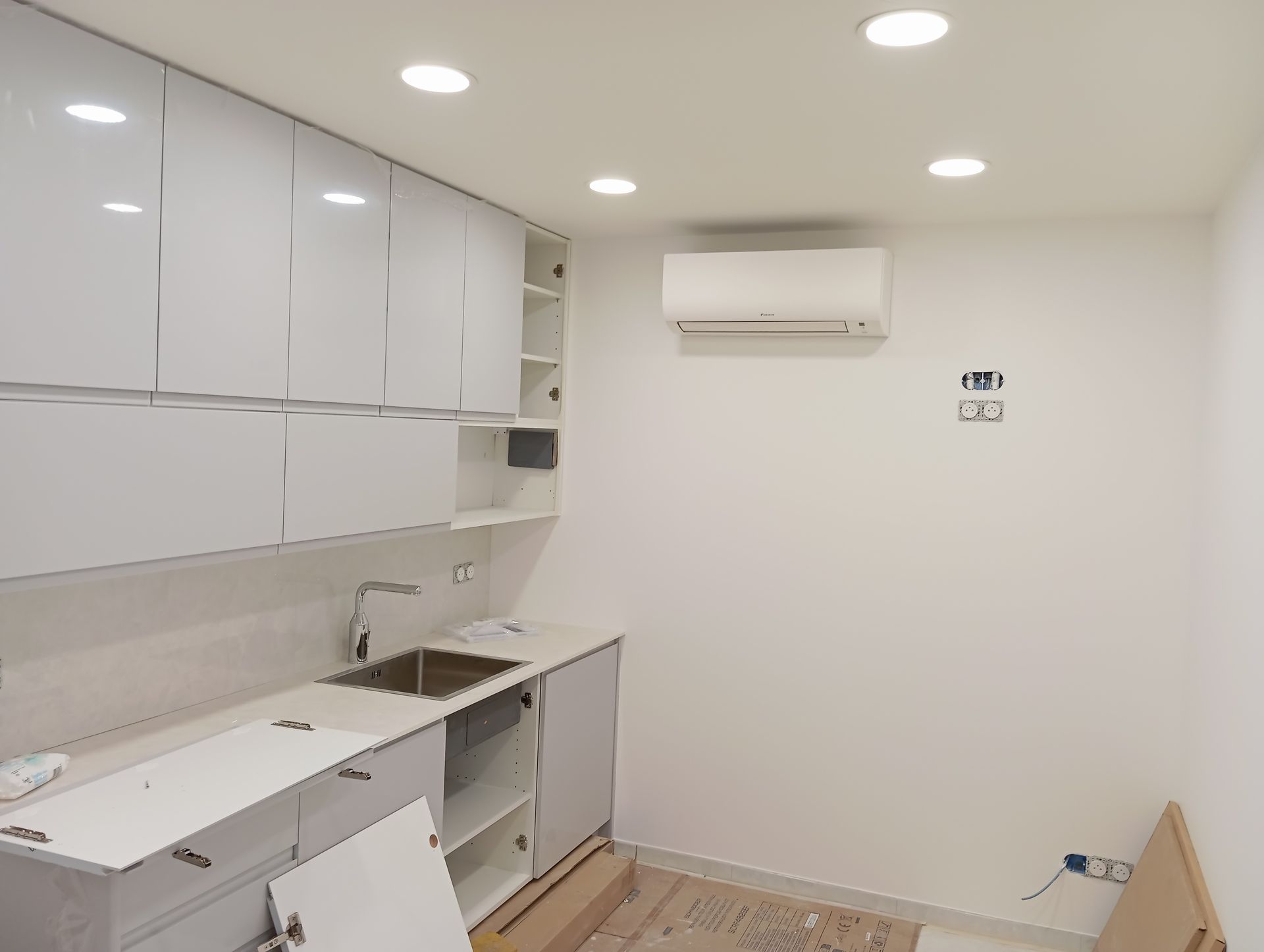 Cuisine blanche avec armoires supérieures, évier et climatiseur au mur.