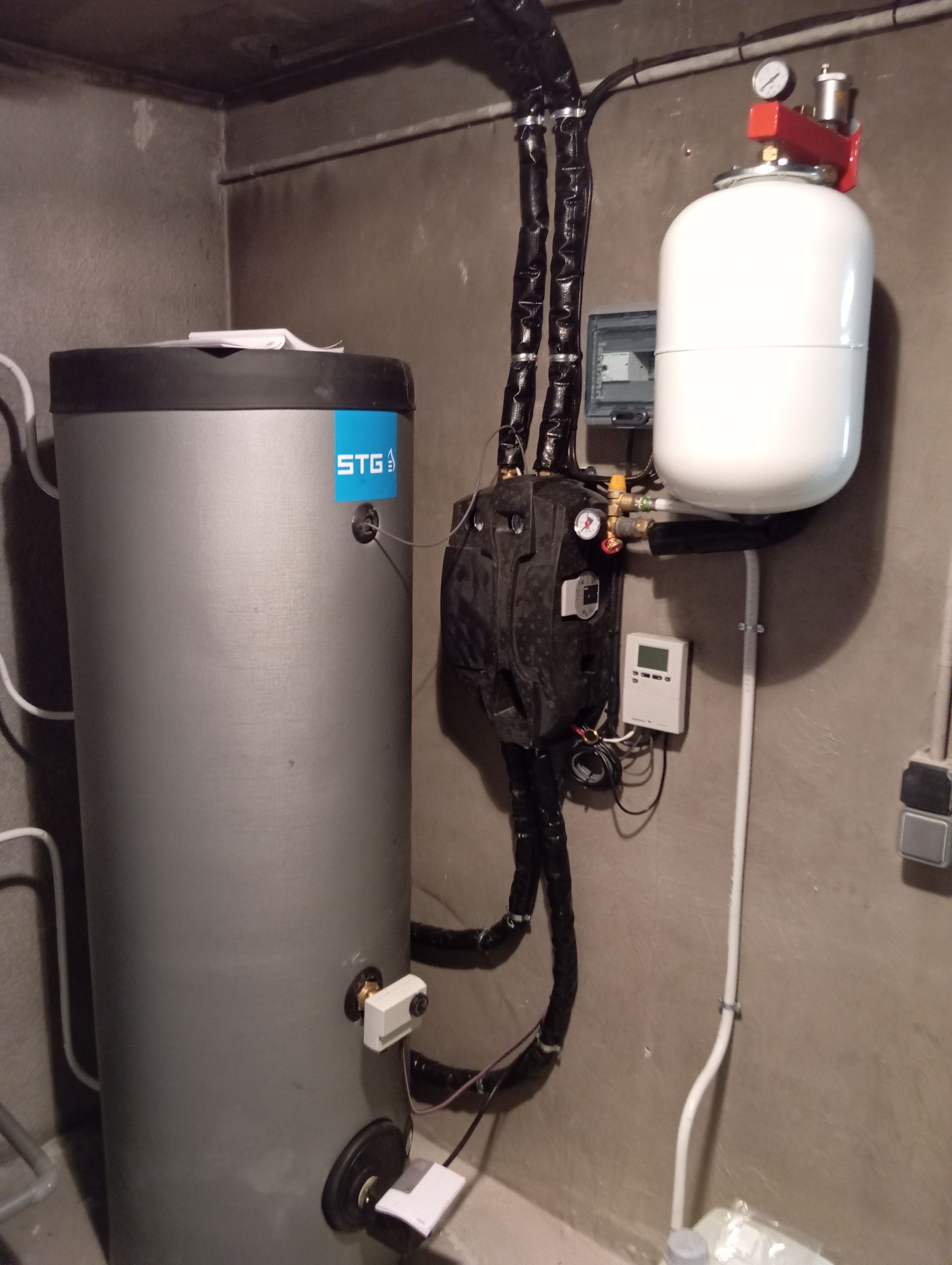 Chauffe-eau gris et vase d'expansion blanc installés sur un mur de béton.