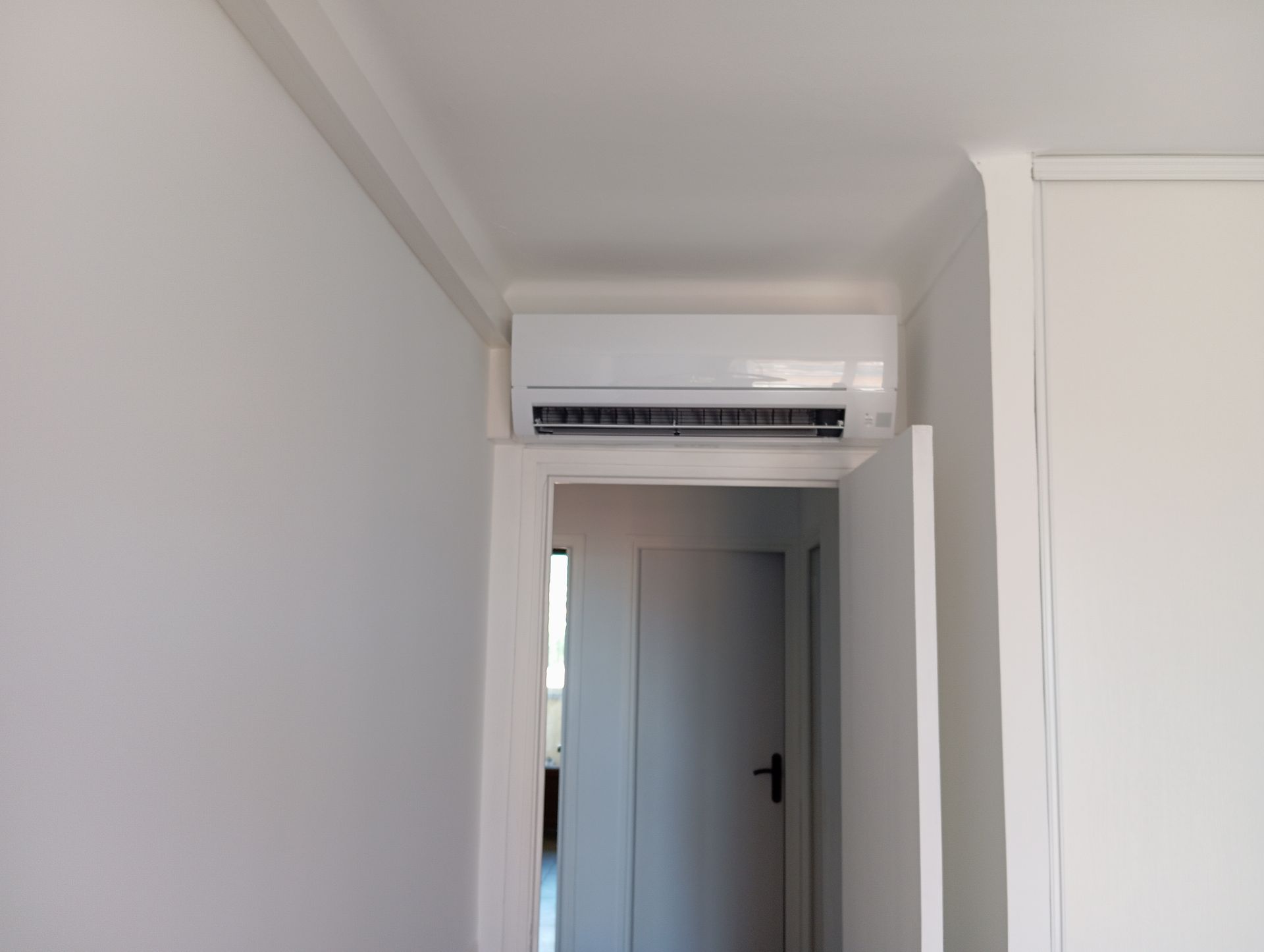 Unité de climatisation blanche montée au-dessus d'une porte dans une pièce blanche.