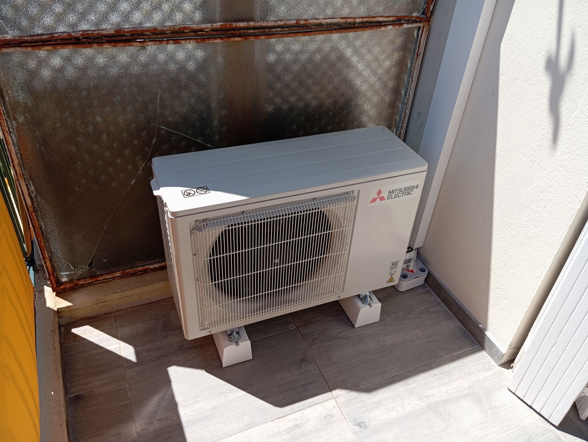Unité de climatisation Mitsubishi sur un balcon, posée sur des blocs de béton.