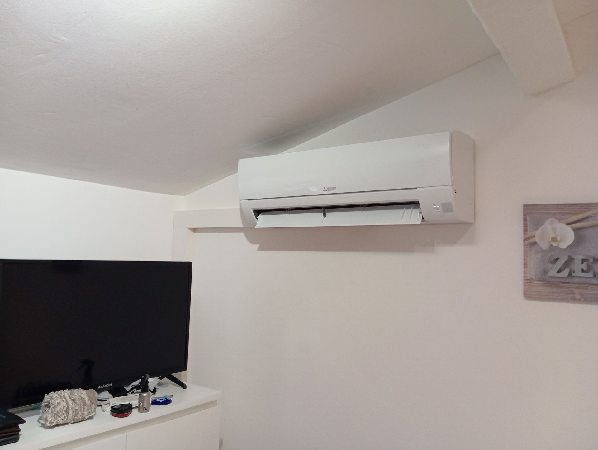 Climatiseur blanc monté sur un mur blanc au-dessus d'une commode blanche avec une télévision et des œuvres d'art.