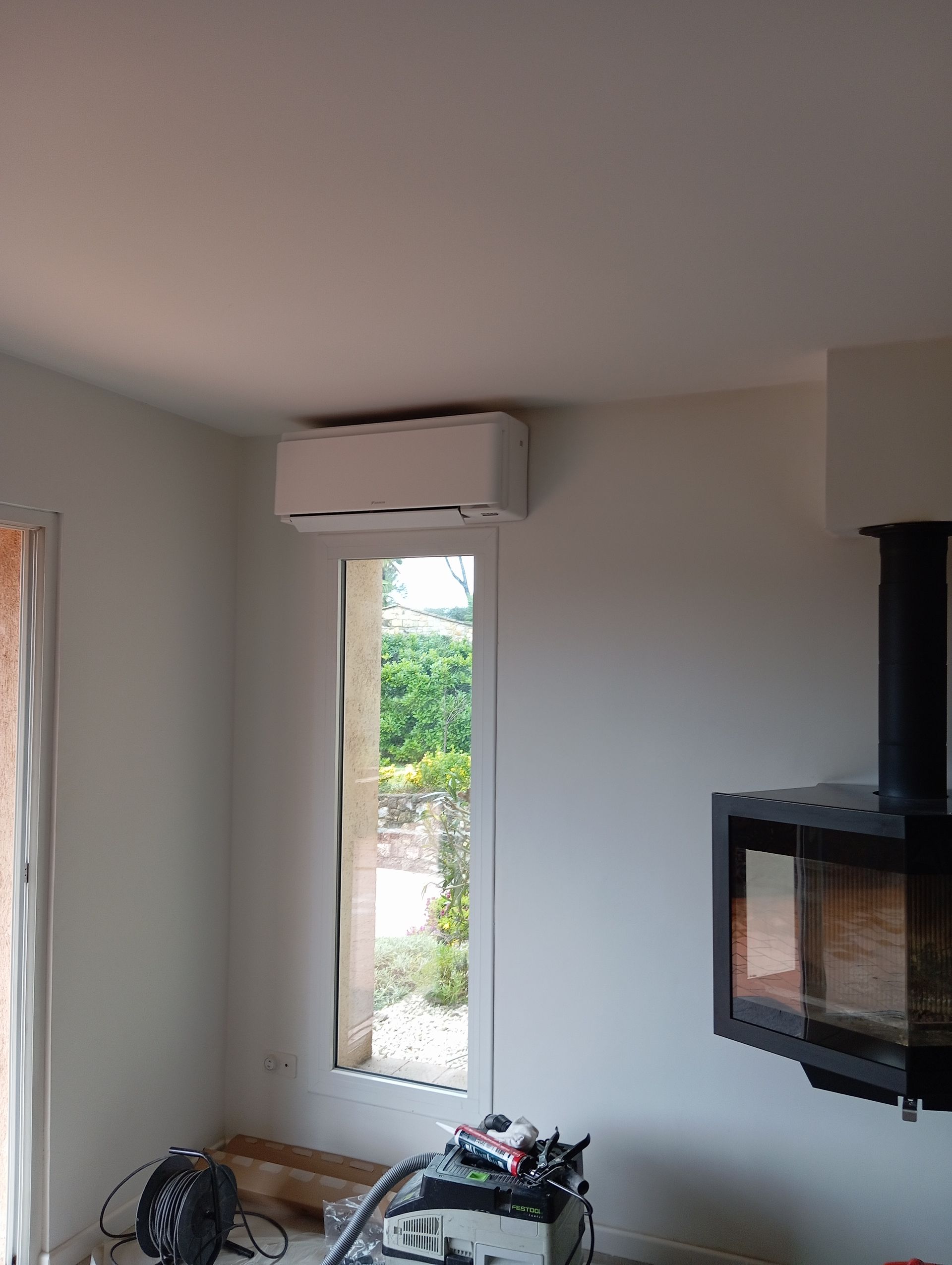 Climatiseur au dessus d'une fenêtre, cheminée à droite, vue intérieure.