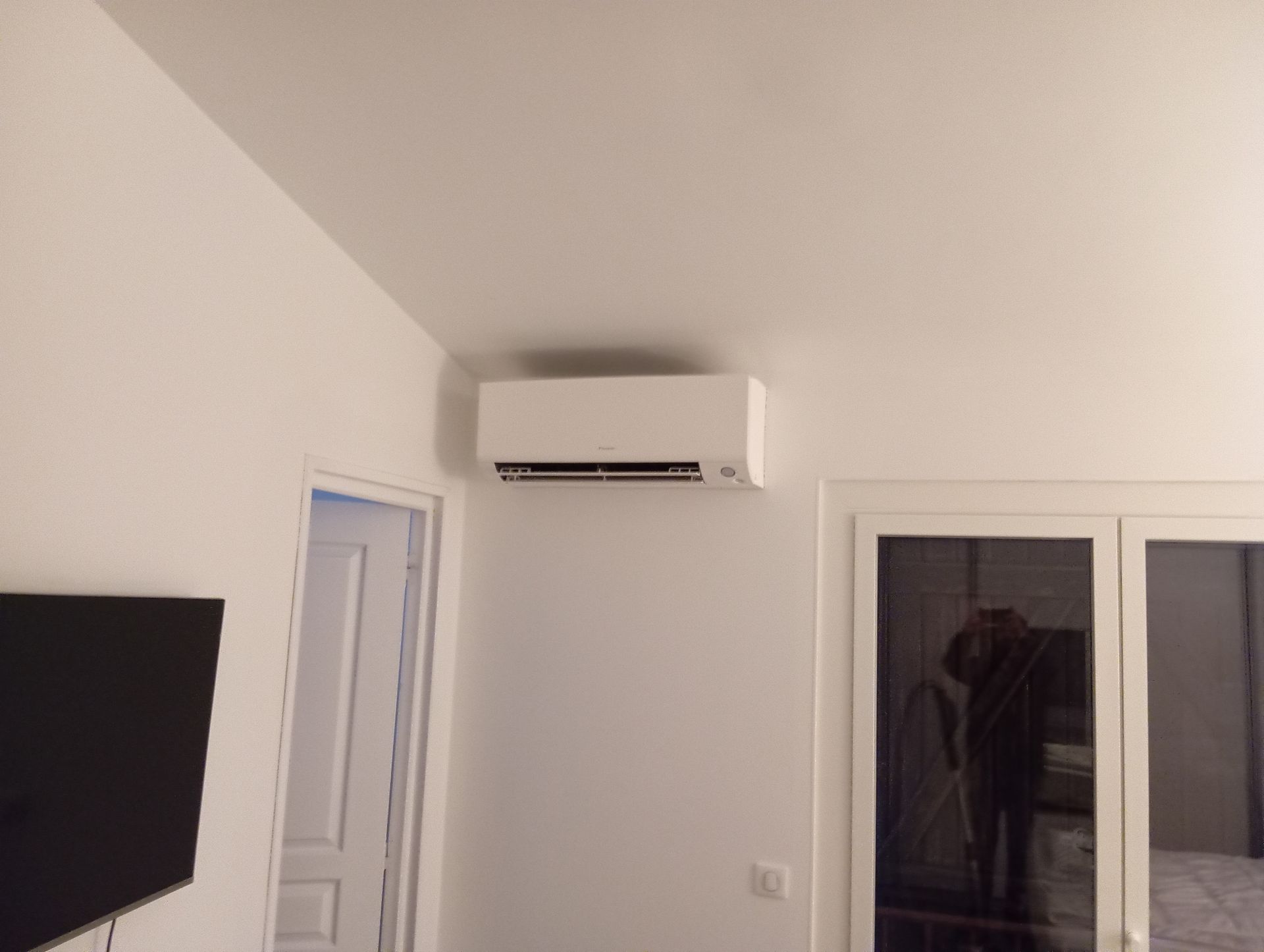 Unité de climatisation blanche montée sur un mur blanc au-dessus d'une porte et de fenêtres.