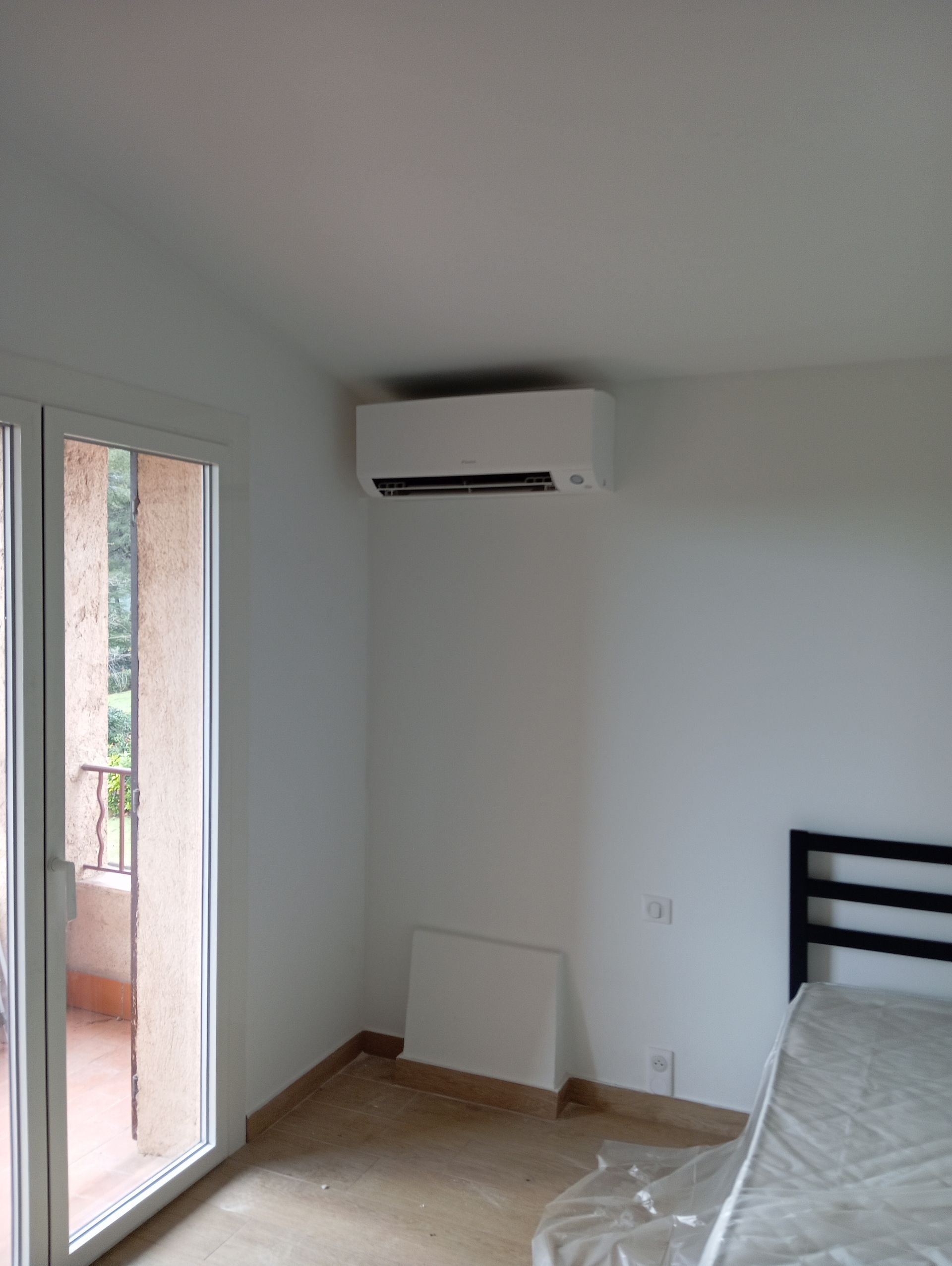 Chambre blanche avec climatiseur, fenêtre et lit.