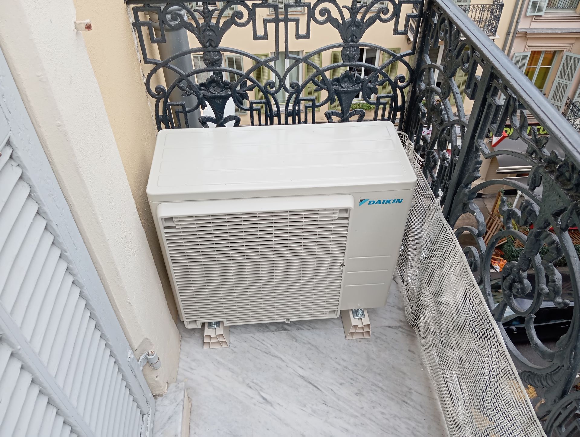 Climatiseur sur un balcon avec balustrade en fer forgé et bâtiment décoratif.