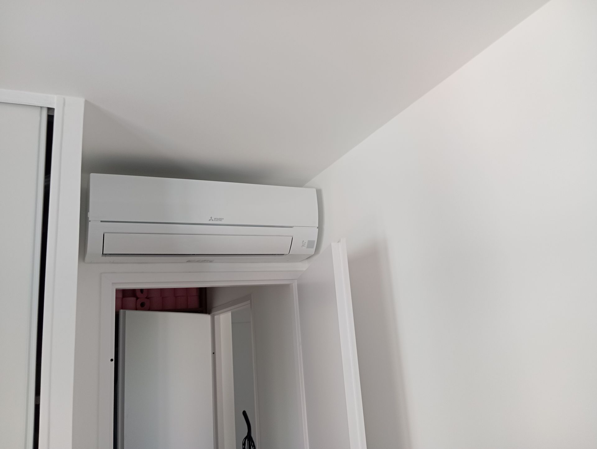 Unité de climatisation blanche au-dessus d'une porte dans une pièce aux murs blancs.
