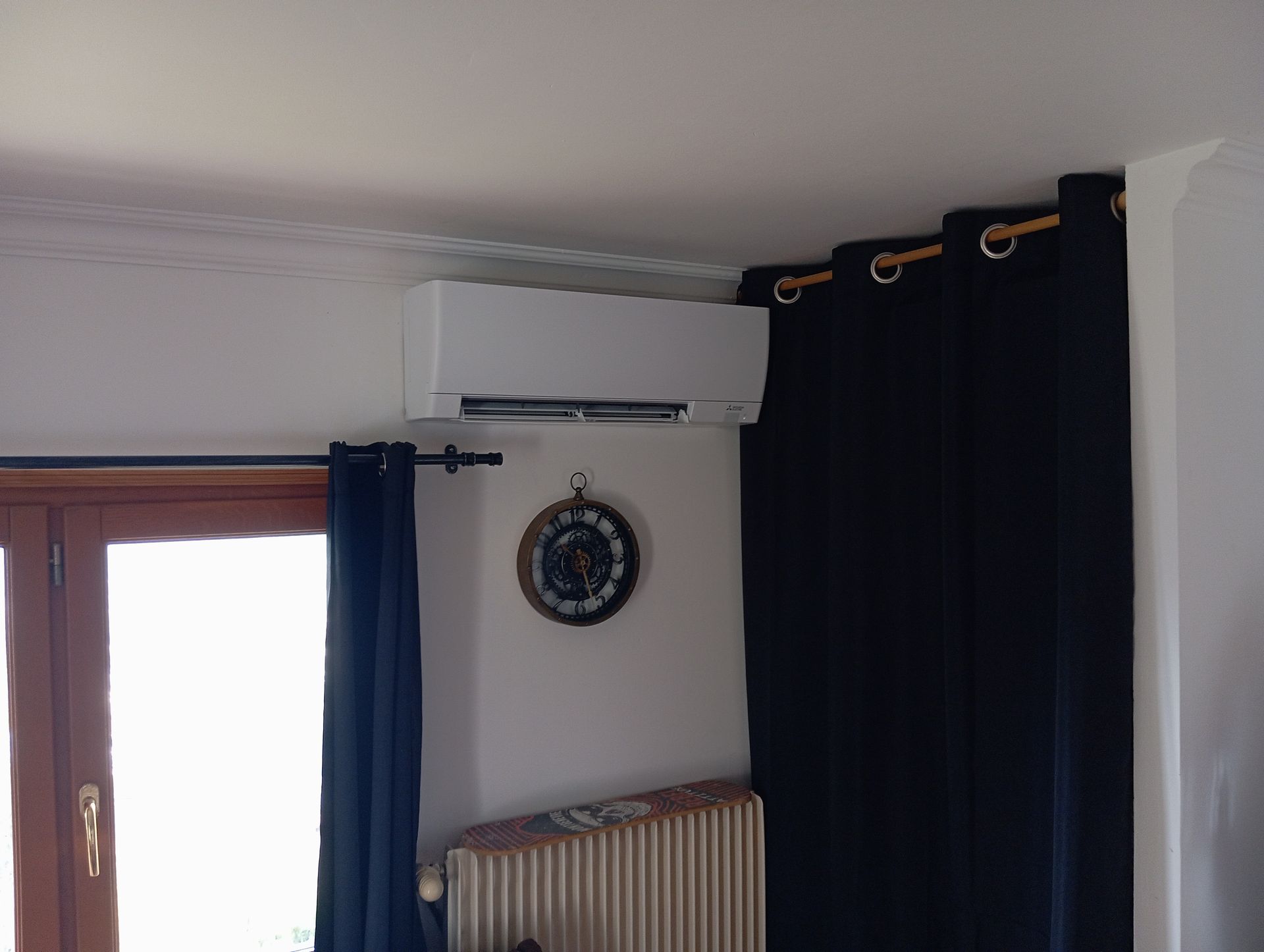 Climatiseur au-dessus d'un radiateur et rideaux bleu foncé dans le coin d'une pièce.