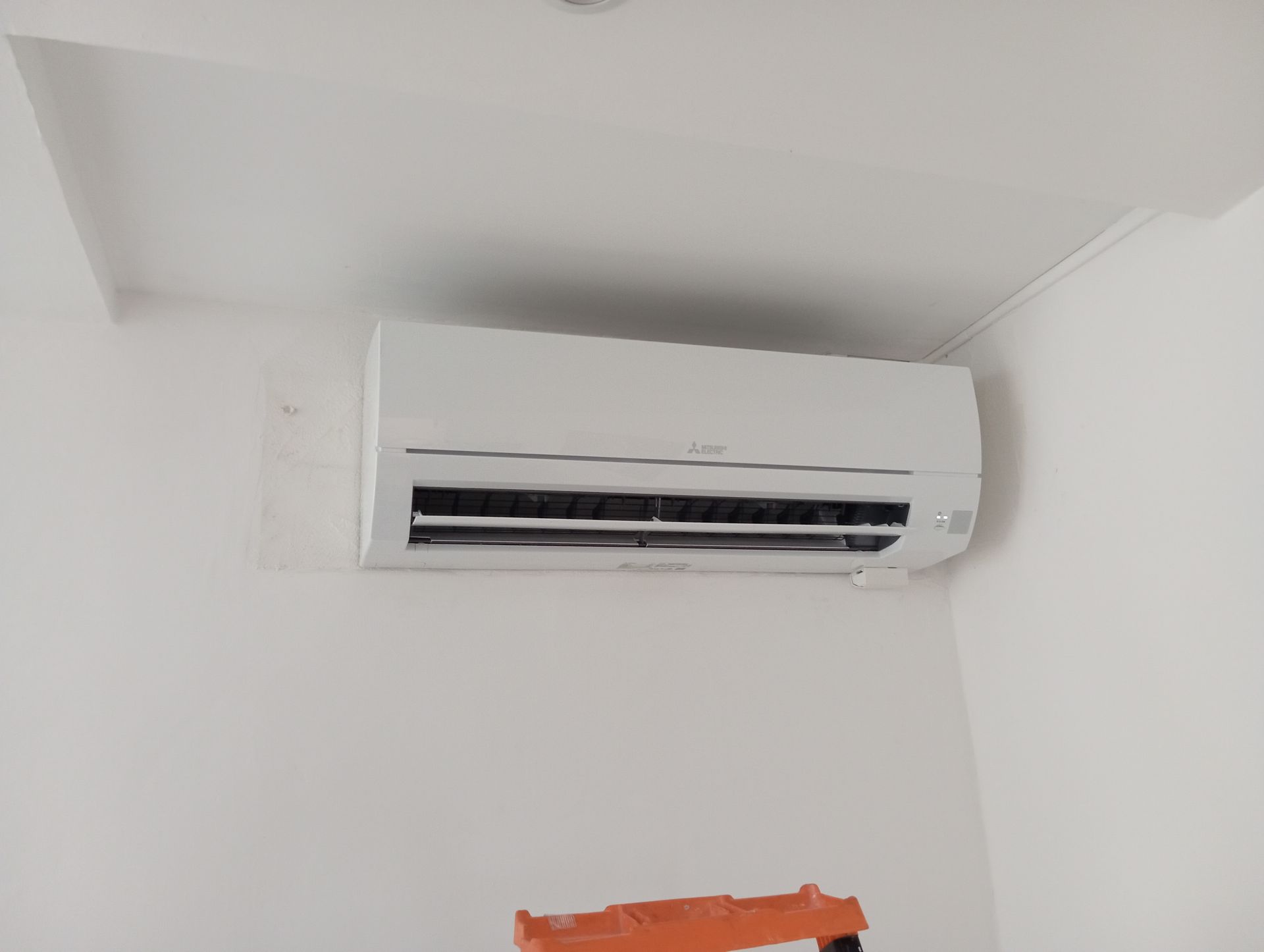 Unité de climatisation blanche montée sur un mur blanc, près d'un coin.